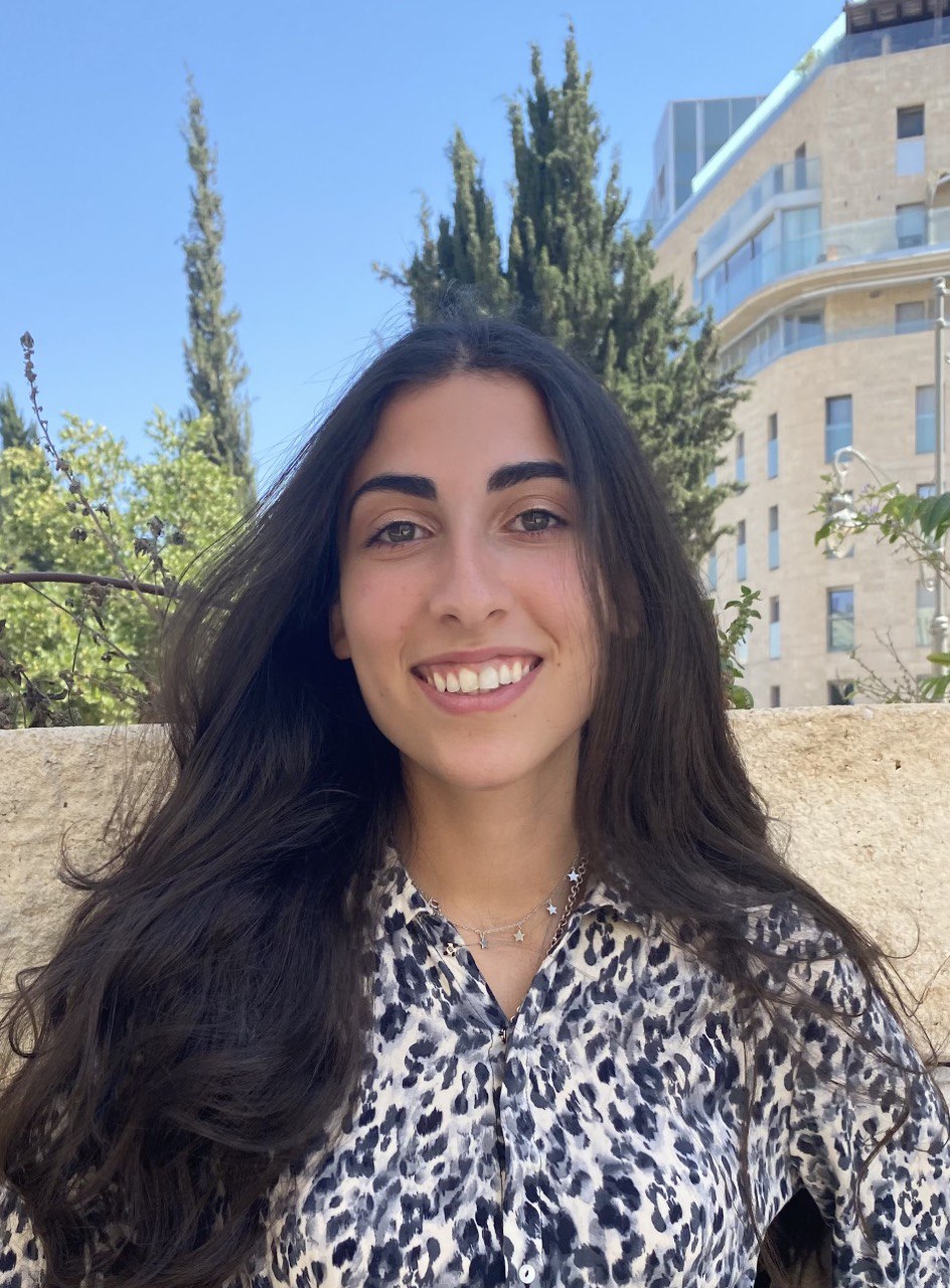 A woman in a leopard print shirt smiles in front of a building.