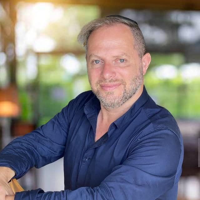 A man in a blue shirt leaning against a table.